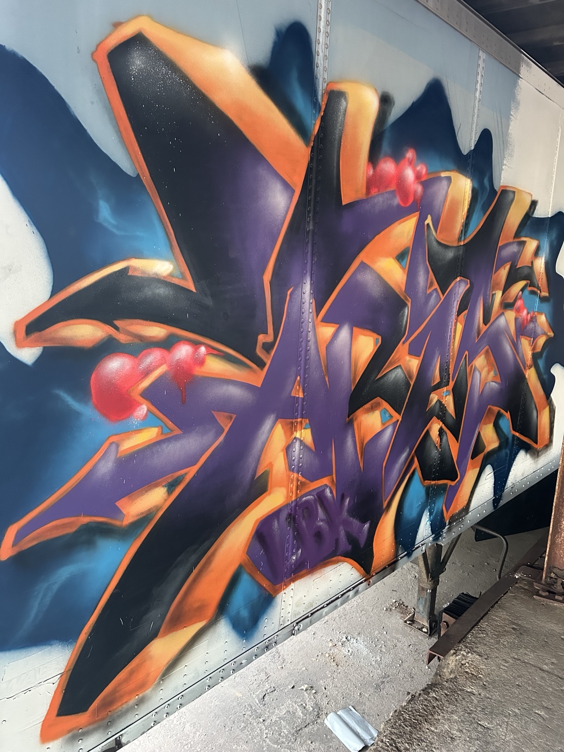 Orange and purple graffiti lettering painted on a trailer